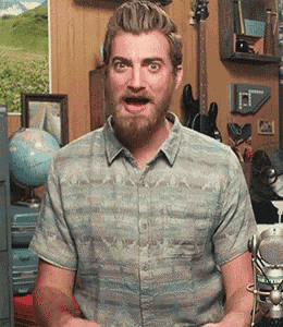 a man with a beard wearing a striped shirt is standing in front of a microphone .