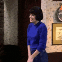 a woman in a blue sweater is standing in front of a picture