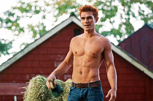 a shirtless man is holding a bale of hay