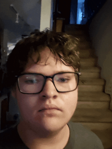 a young man wearing glasses looks at the camera