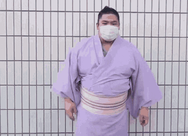 a sumo wrestler in a purple kimono is standing in front of a tiled wall .