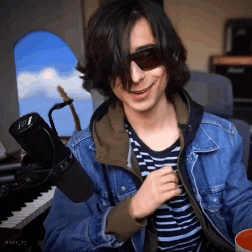 a young man wearing sunglasses and a denim jacket is smiling