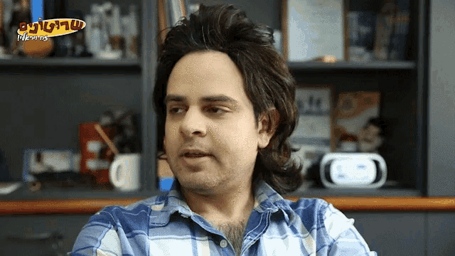 a man in a blue plaid shirt is sitting in front of a shelf with a sign that says ' itunes '