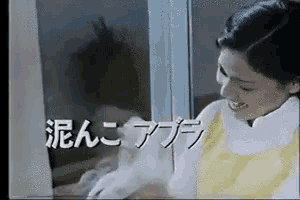 a woman in a yellow apron is smiling while cleaning a window in a video .