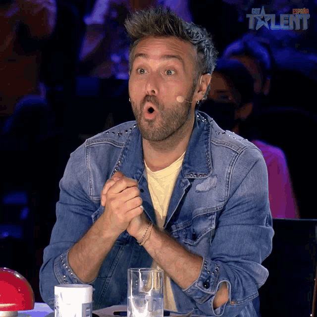 a man in a denim jacket is sitting at a table with a glass of water in front of him and the word talent on the bottom