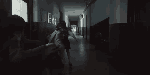 a couple of girls are running down a hallway in a dark room