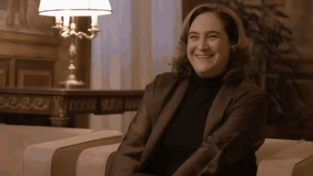 a woman sits in a chair smiling in front of a table that says ' a ' on it