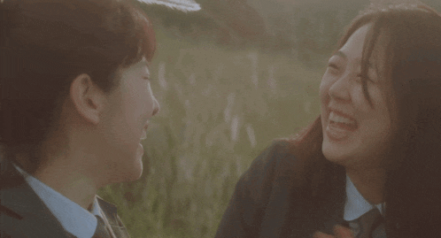 two girls are laughing in a field and one has a feather on her head