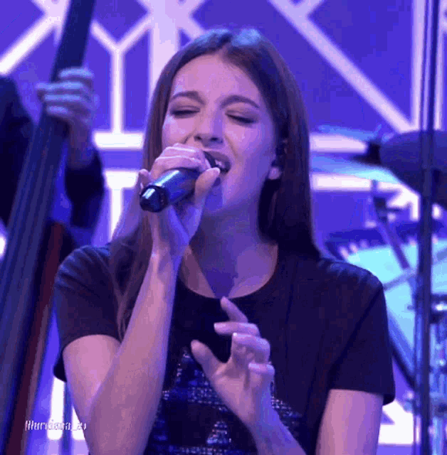 a woman is singing into a microphone on a stage with a blue background