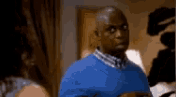 a man in a blue sweater is standing in front of a camera .