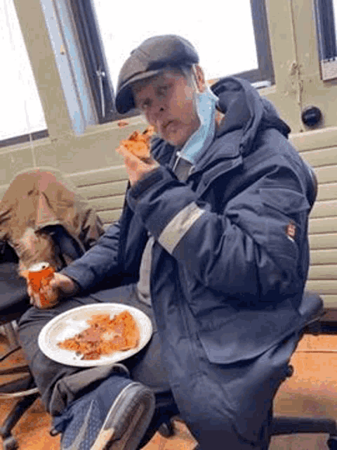 a man is sitting in a chair eating a slice of pizza .