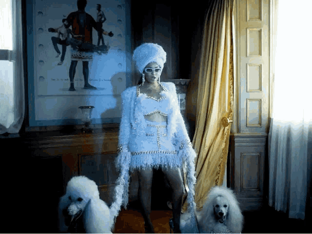 a woman standing next to two white poodles in front of a painting