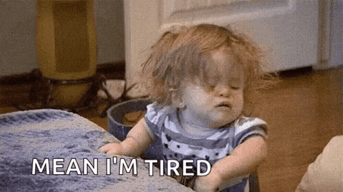 a little girl is sitting on a bed with her eyes closed and the words `` mean i 'm tired '' next to her .