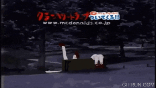 two anime characters are sitting on a bench in front of a mcdonald 's ad