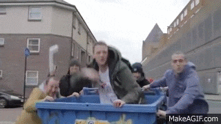 a group of people are pushing a blue dumpster on a street .
