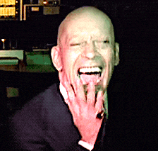 a bald man in a suit and tie is laughing with his hand on his face