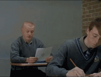 a man is throwing a piece of paper at another man who is writing