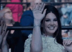a woman in a white dress is sitting in a crowd and waving her hand .