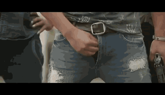 a man wearing ripped jeans and a belt is standing in a crowd .