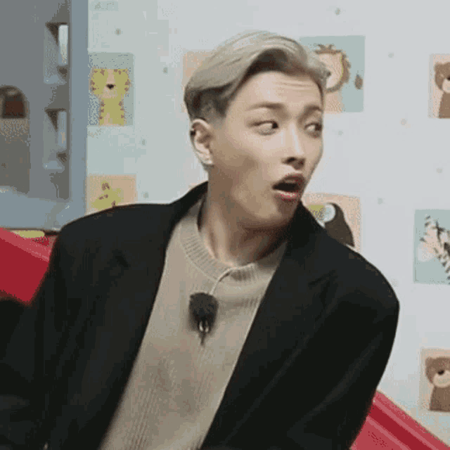 a man in a suit and sweater is making a funny face while sitting on a red chair .