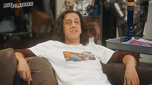 a man sitting on a couch wearing a shirt that says ' bit playas ' on it