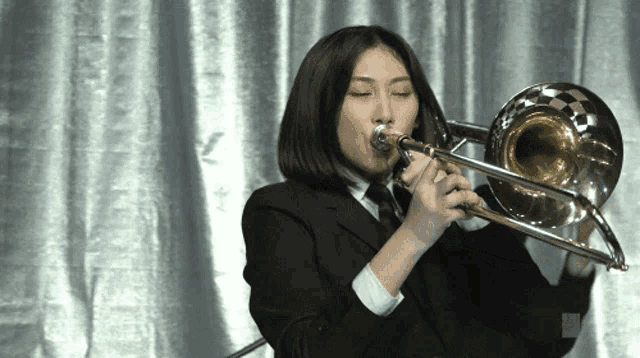 a woman playing a trombone in front of a silver curtain