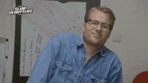 a man wearing glasses and a blue shirt is smiling in front of a sign that says sluip schufters