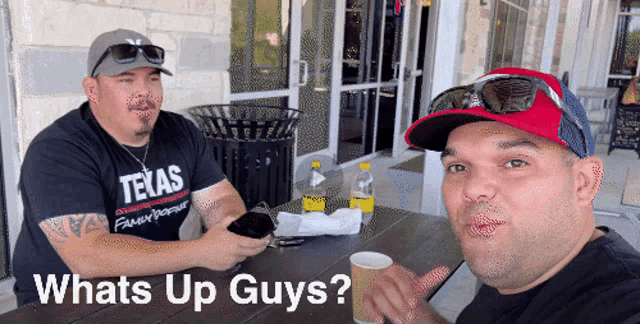 two men sit at a table with the words whats up guys