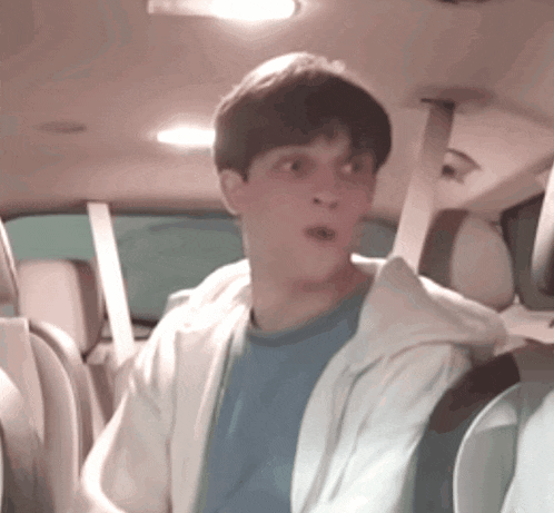 a young man in a blue shirt is sitting in the back seat of a car