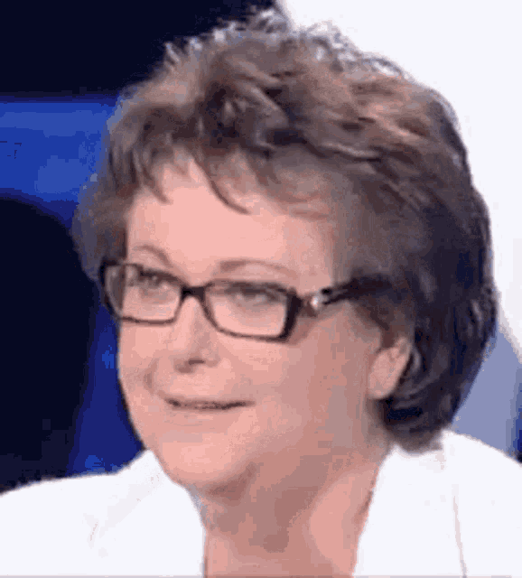 a woman wearing glasses is smiling and wearing a white shirt .
