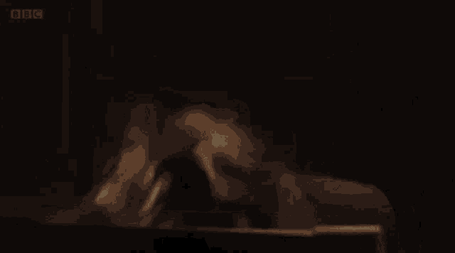 a man with a mustache is sitting in a dark room looking at a laptop .