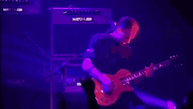 a man is playing a guitar in front of a purple amp .