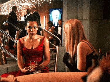 a woman in a red dress sits at a table talking to another woman in a black dress