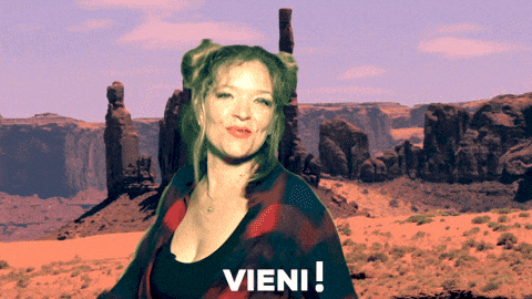a woman in a plaid shirt stands in front of a desert landscape and says " vieni "