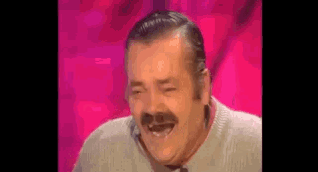 a man with a mustache is laughing while sitting on a stage .