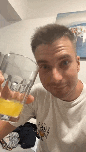 a man in a white shirt is holding a glass of orange juice in his hand