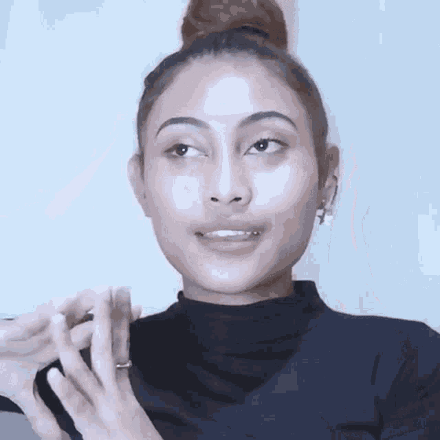a woman with her hair in a bun is wearing a black turtleneck sweater and earrings .