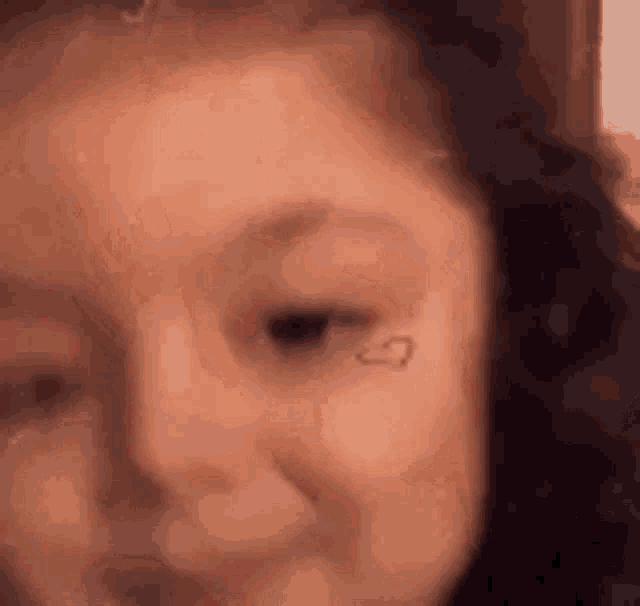 a close up of a woman 's face with a heart tattoo on her face .