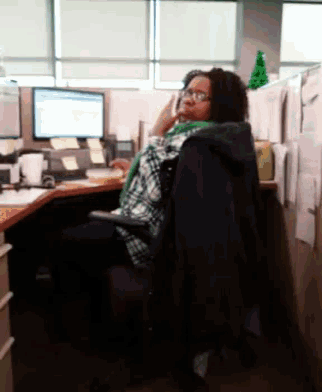 a woman sits at a desk in front of a computer talking on a cell phone