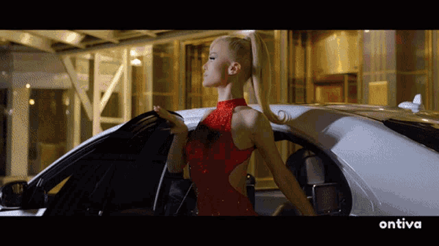 a woman in a red dress is standing next to a white car with the word ontiva on the bottom