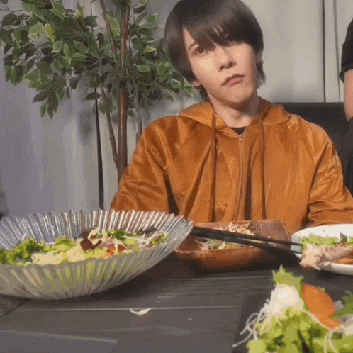 a young man sitting at a table with plates of food and chopsticks