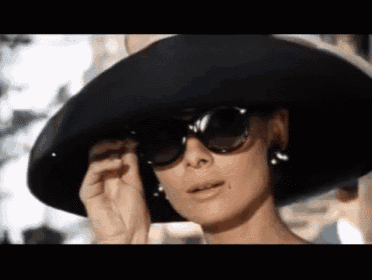 a woman wearing sunglasses and a hat is adjusting her sunglasses .