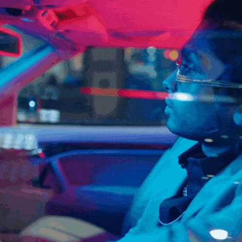 a man wearing glasses and a necklace is driving a car at night