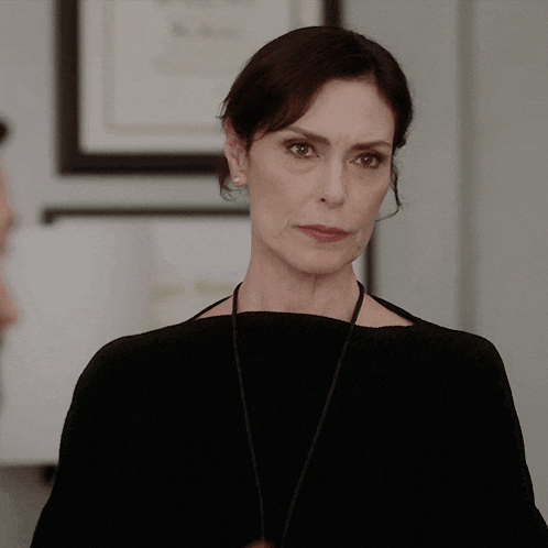 a woman wearing a black sweater and a necklace smiles