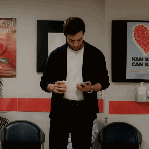 a man in a suit looks at his phone in front of a poster that says kan b can b