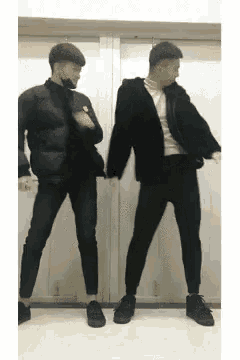 two men are standing next to each other dancing in front of a white wall .