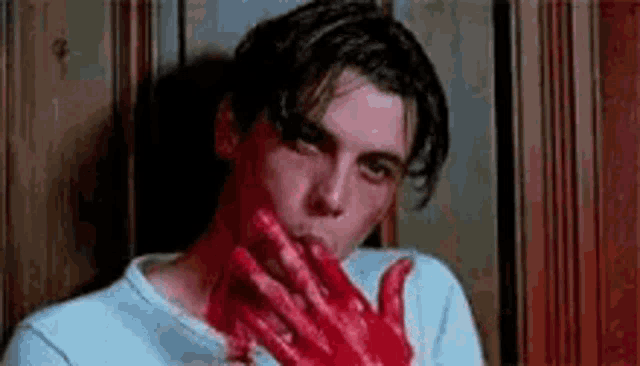 a man is holding a bloody hand in front of his mouth .