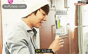 a man in a white hat is standing in front of a refrigerator and holding a piece of food .