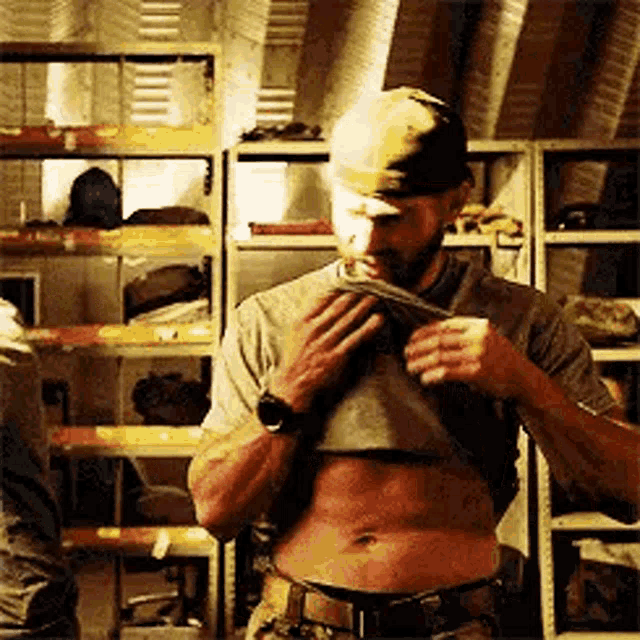 a man with a beard is taking off his shirt in a room with shelves .