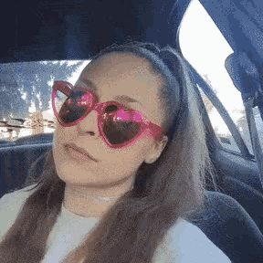 a woman wearing pink heart shaped sunglasses sitting in a car